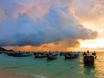 Boats moored in sea against sky during sunset