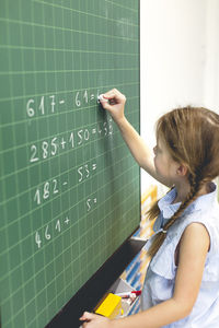 Girl solving mathematics equation on blackboard in classroom at school