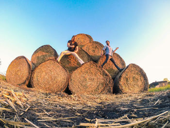 Friends standing on hay bales stack against clear sky