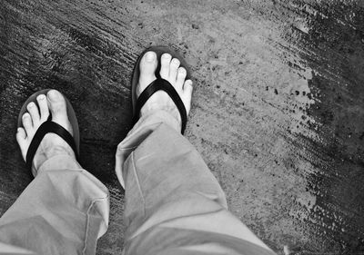 Low section of person wearing flip-flop standing on wet footpath