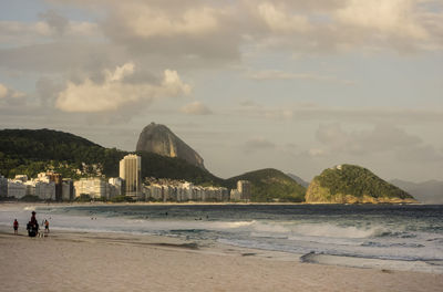 Scenic view of sea by city and mountain against sky