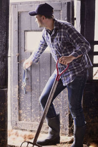 Full length of farmer with pitchfork closing barn door