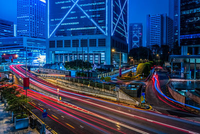 Light trails on road by illuminated buildings in city at night