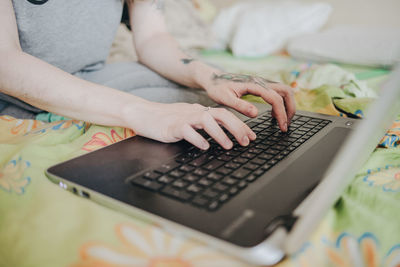 Midsection of woman using laptop while sitting on bed at home