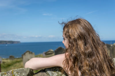 Side view of woman looking at sea against blue sky