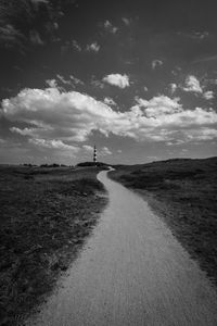 Dirt road on field against sky