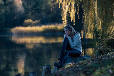 Full length of woman sitting by lake in forest