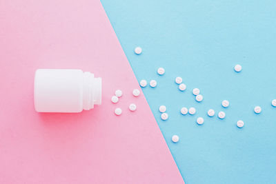 High angle view of pills spilling from bottle against blue background