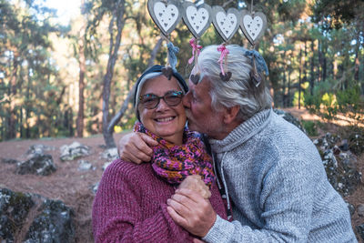 Senior man kissing happy woman in forest