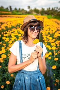 Smiling young woman standing amidst flowering plants on field