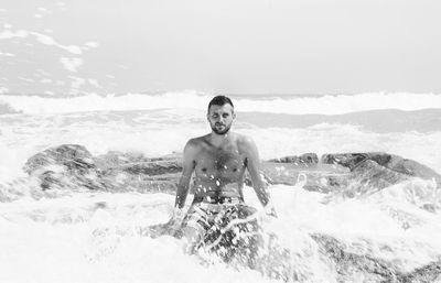 Portrait of shirtless man sitting on rocky shore