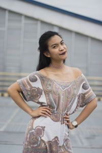 Portrait of young woman with hands on hip standing in city