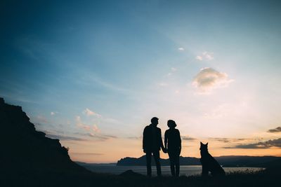 Silhouette friends standing on land against sky during sunset