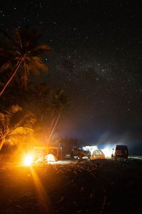 Cars on illuminated street amidst field against sky at night