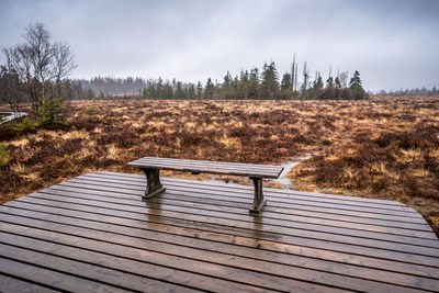 Empty bench in park against sky