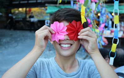 Smiling boy holding colorful floral patterned papers outdoors