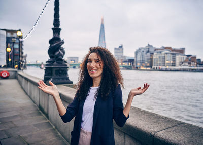 Portrait of woman gesturing while standing against thames river in city