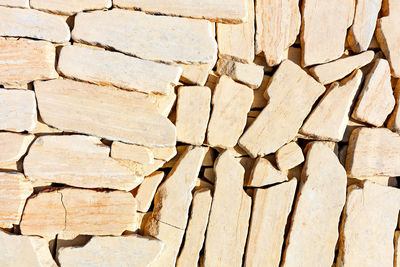 Texture of layered pieces of yellow sandstone stone in harsh sunlight separated by stripes. 