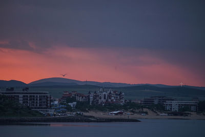 Buildings by sea against sky at sunset