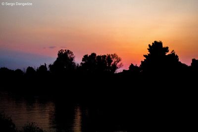 Silhouette trees by lake against sky during sunset