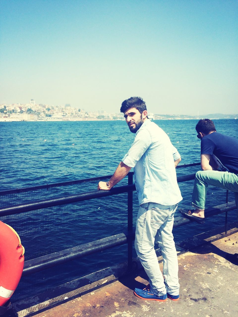 clear sky, sea, water, lifestyles, copy space, leisure activity, casual clothing, horizon over water, transportation, beach, standing, sitting, young adult, person, railing, shore, full length, sunglasses