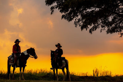 Three men dressed in cowboy garb, with horses and guns. a cowboy riding a horse in the sunset.