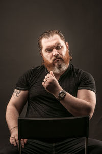 Portrait of man sitting against black background