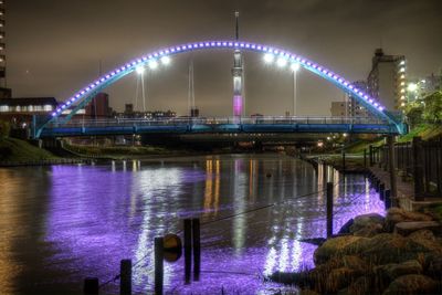 Illuminated bridge over river against sky in city at night