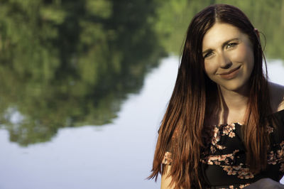 Portrait of smiling young woman sitting against lake