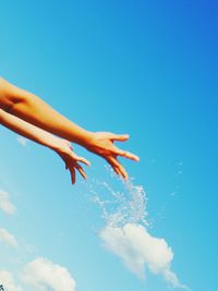 Close-up of hand splashing water against blue sky