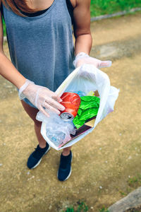 Low section of woman putting drink can in plastic bag at park