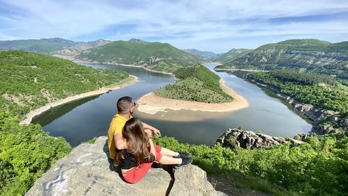 Woman sitting on mountain by lake against mountains