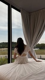 Rear view of woman sitting on bed at home