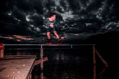 Man surfing on railing over sea against sky at night