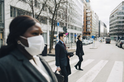 Female and male colleagues crossing street in city during pandemic