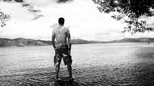 Rear view of man standing on shore against sky