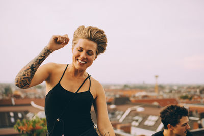 Excited woman dancing while enjoying with friend on terrace against sky