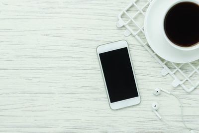 High angle view of coffee cup by mobile phone and headphones on table