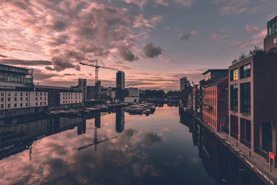 Canal amidst buildings against cloudy sky during sunset