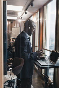 Side view of bald male entrepreneur using laptop in board room seen through glass wall