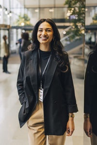 Portrait of happy young businesswoman standing with hand in pocket at convention center