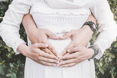 Cropped hands of man touching pregnant woman belly at park