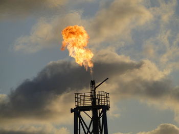 Oil refinery flare stack against cloudy sky