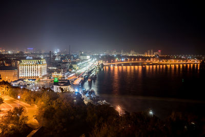 High angle view of illuminated bridge over river by buildings in city at night