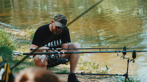 Man adjusting fishing rod while crouching by lake