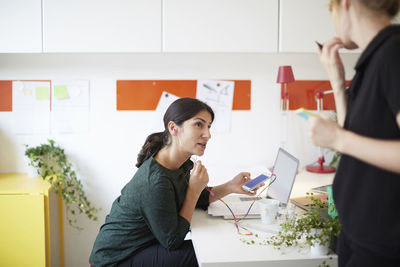 Businesswoman using hands-free device while looking at colleague in office