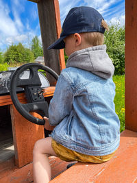 Little boy pretending driving wooden car on rural playground