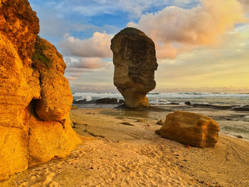 Rock formation on beach against sky during sunset