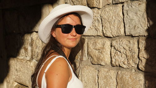Portrait of woman wearing sunglasses standing against wall