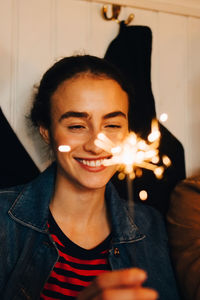 Smiling young woman holding sparkler while enjoying dinner party at restaurant